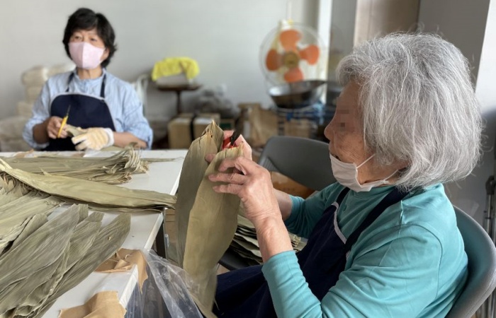 圖說:阿嬤幫忙剪粽葉,跟志工們一起義賣素粽。(攝影:吳惠珍)